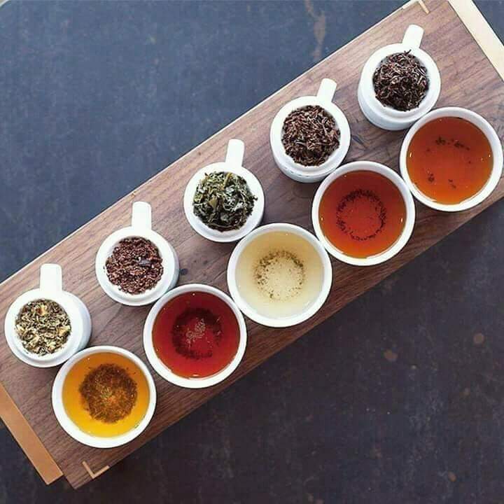 A flight of tea liquors and dry leaf samples on a wooden board